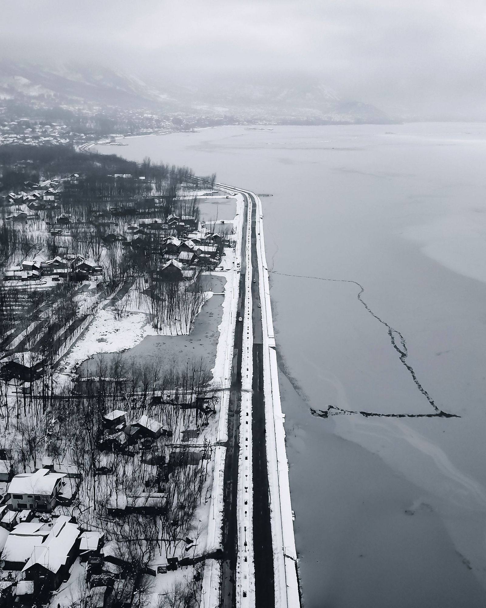 Aerial view of a frozen Dal Lake with snow on its banks