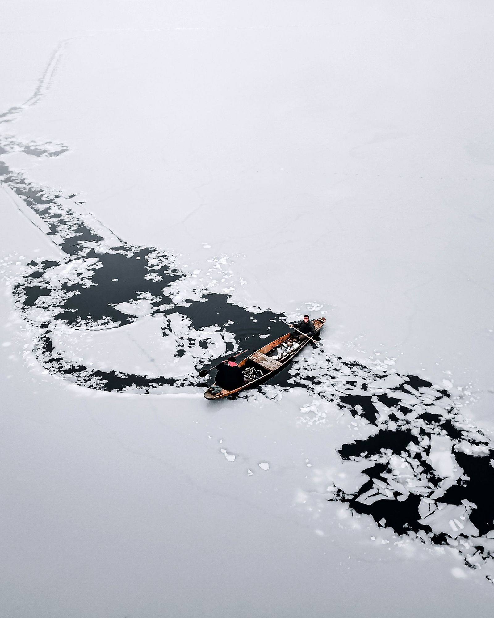 A wooden boat cutting a path through the frozen Dal Lake