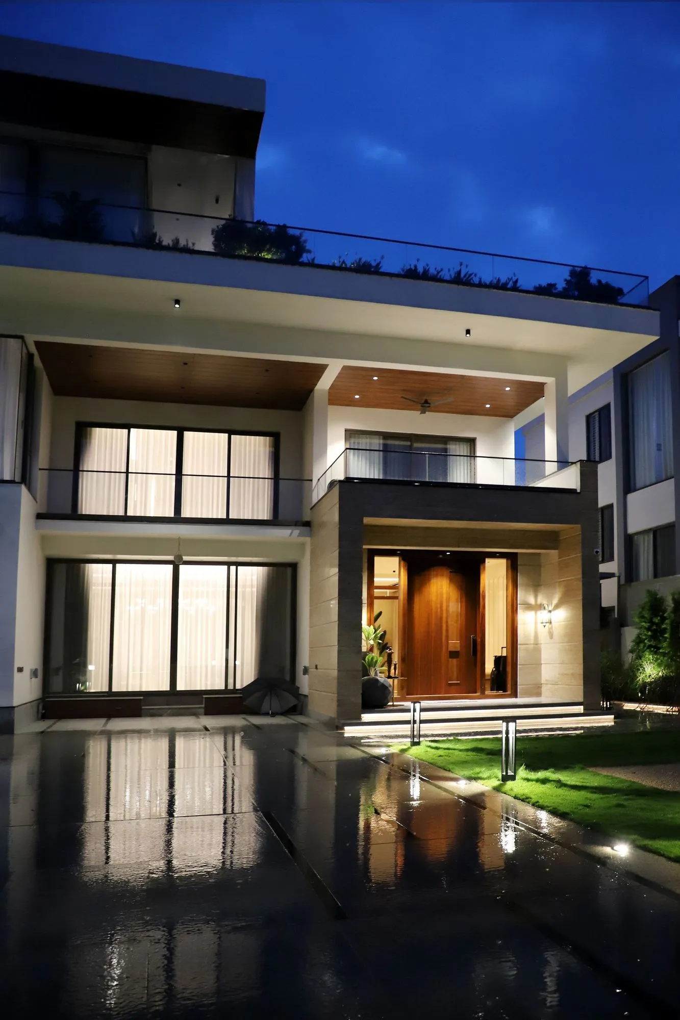 A two-storey contemporary house with large glazed openings lit at dusk