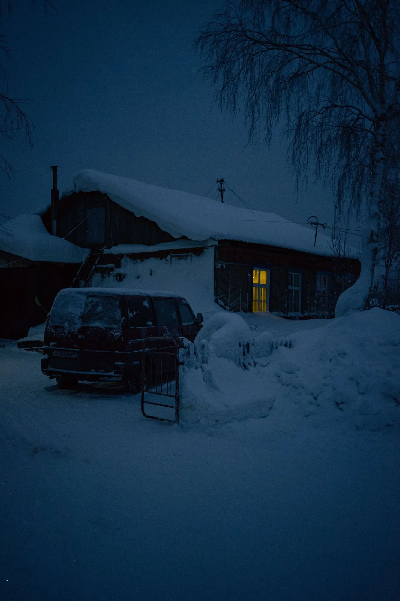 A house and parked vehicle surrounded by deep snow at night