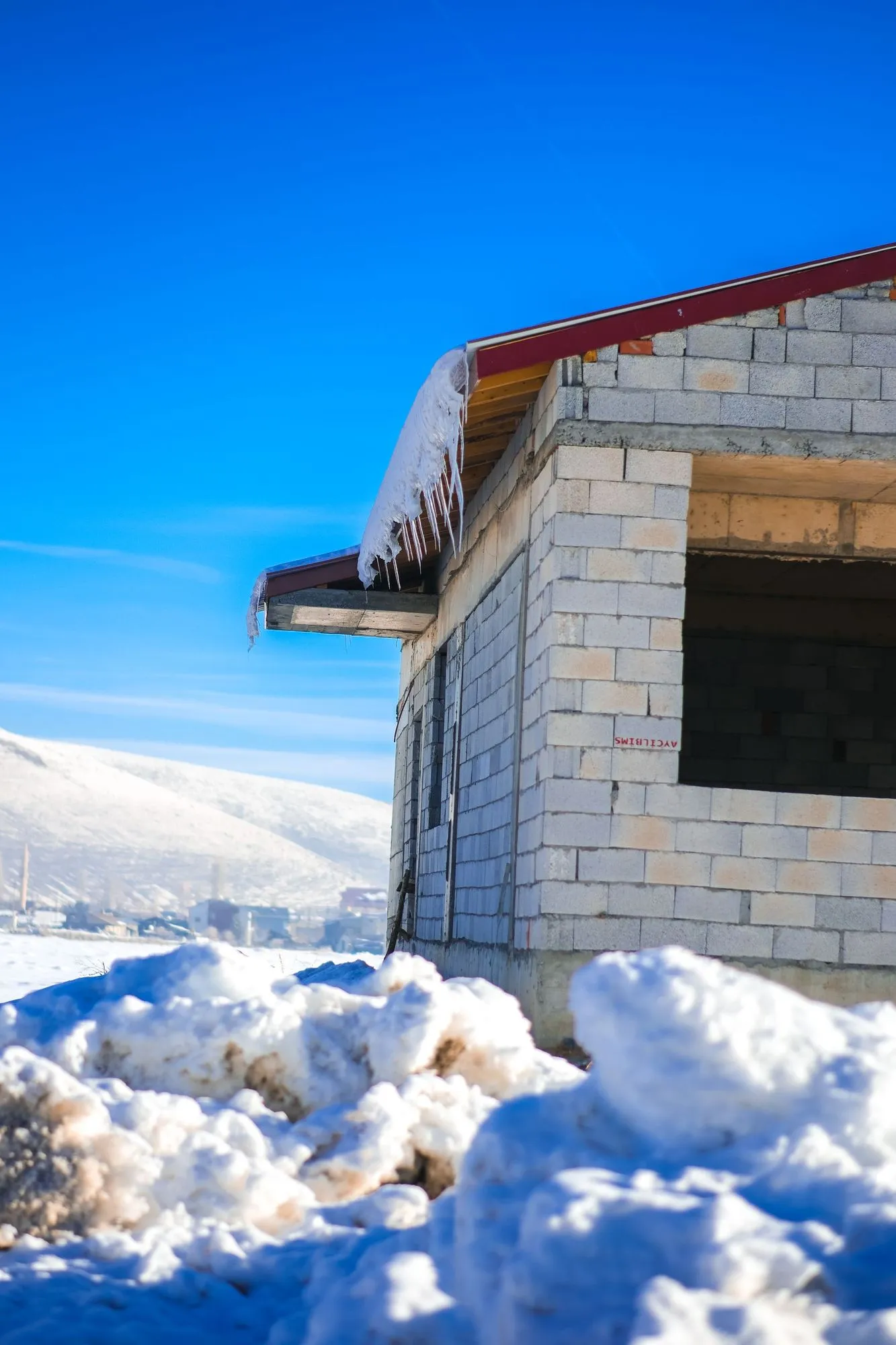 Snow resting on the projecting edge of a roof above an unfinished masonry wall