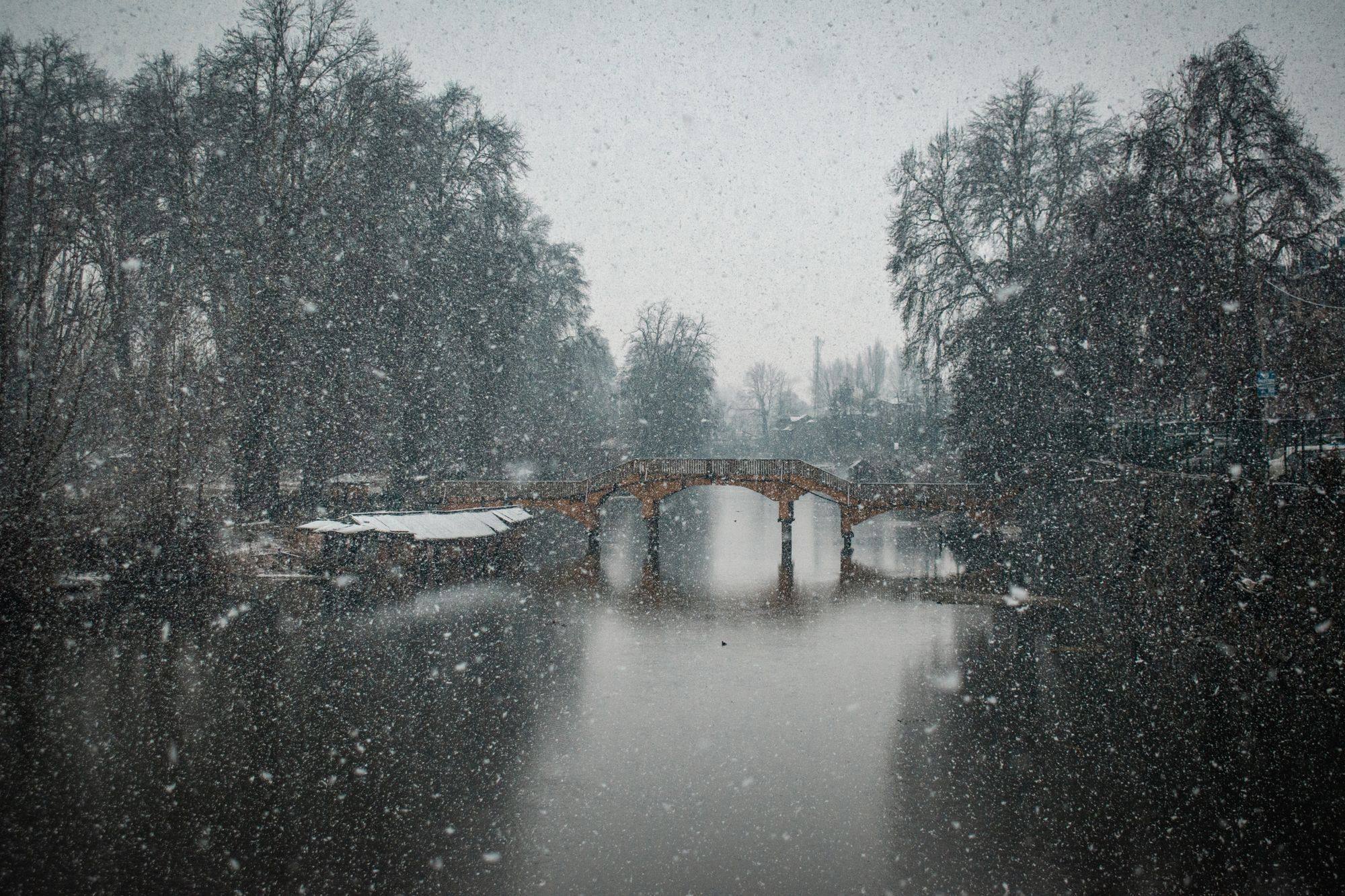 Snow falling on a bridge over a river in Srinagar